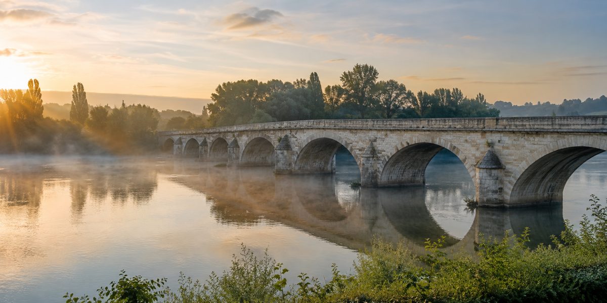 Pont de pierre ancien traversant une rivière au lever du jour